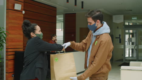Deliveryman-in-Mask-and-Gloves-Giving-Paper-Bag-to-Businesswoman